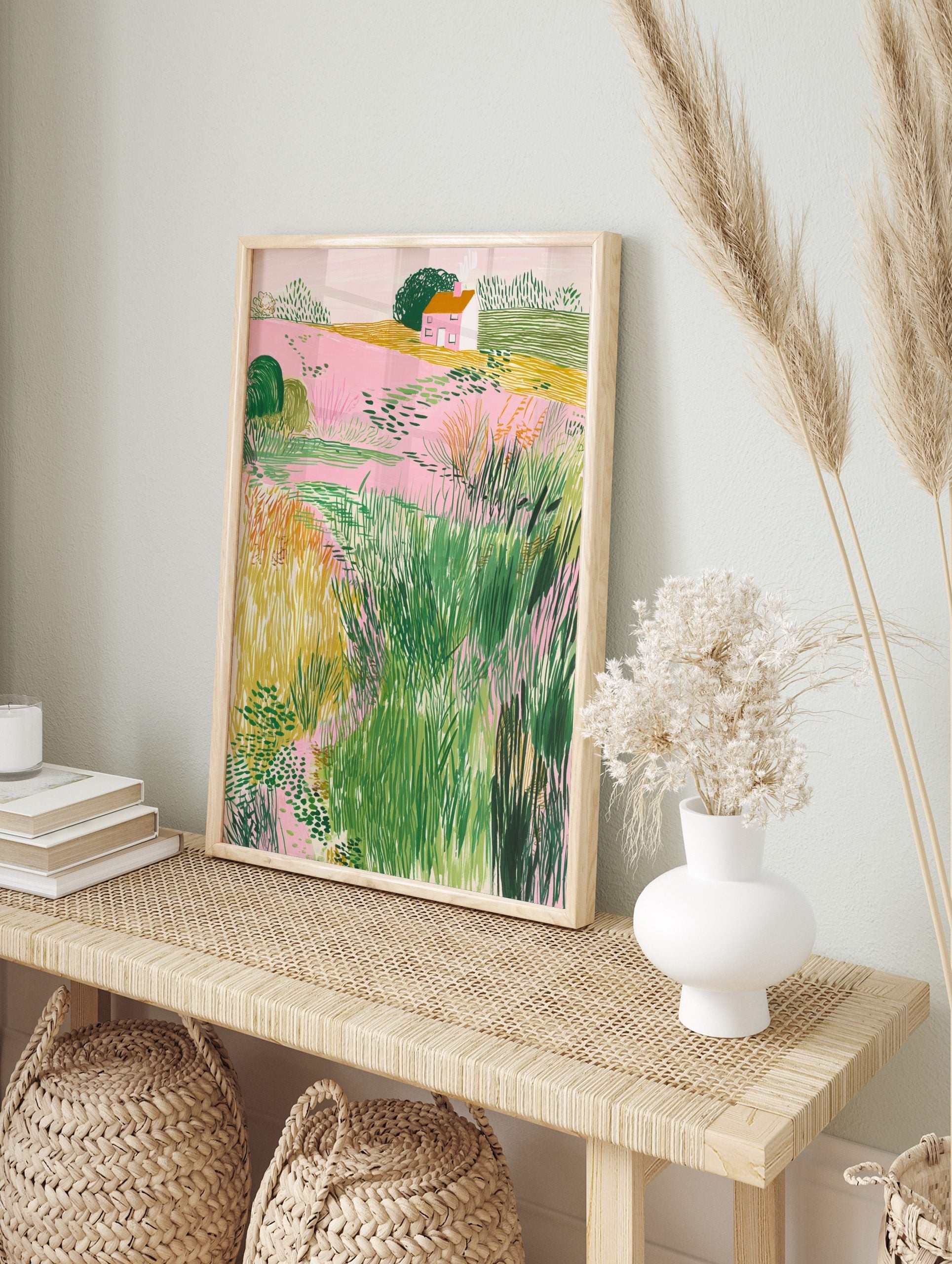 Illustrative landscape art print with pink fields, green bushes, yellow grass, and a small, in an alternate framed mockup