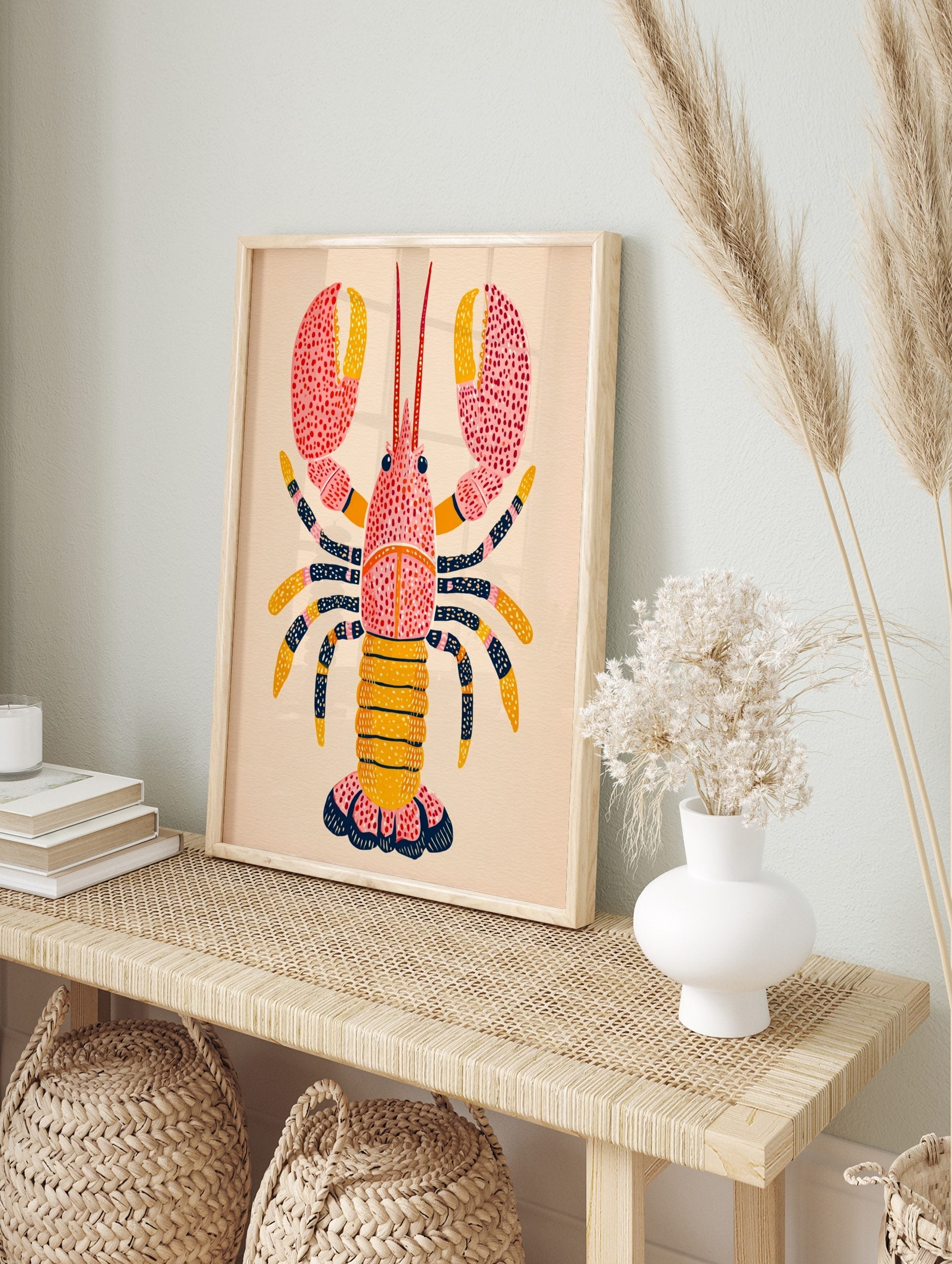Illustrative pink and yellow lobster wall art print with dark blue patterned legs and red dots, in an alternate framed mockup