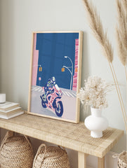 Illustrative print of a rider on a pink sports motorbike with Japanese text, on a deep blue, in an alternate framed mockup