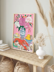 Still life illustration of red lobster, oysters, lemons, and pink flowers in blue vase on, in an alternate framed mockup