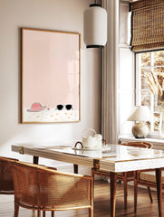 Illustrative print of a pink sun hat, black sunglasses, and red starfish on sand with a peach, in a styled room mockup