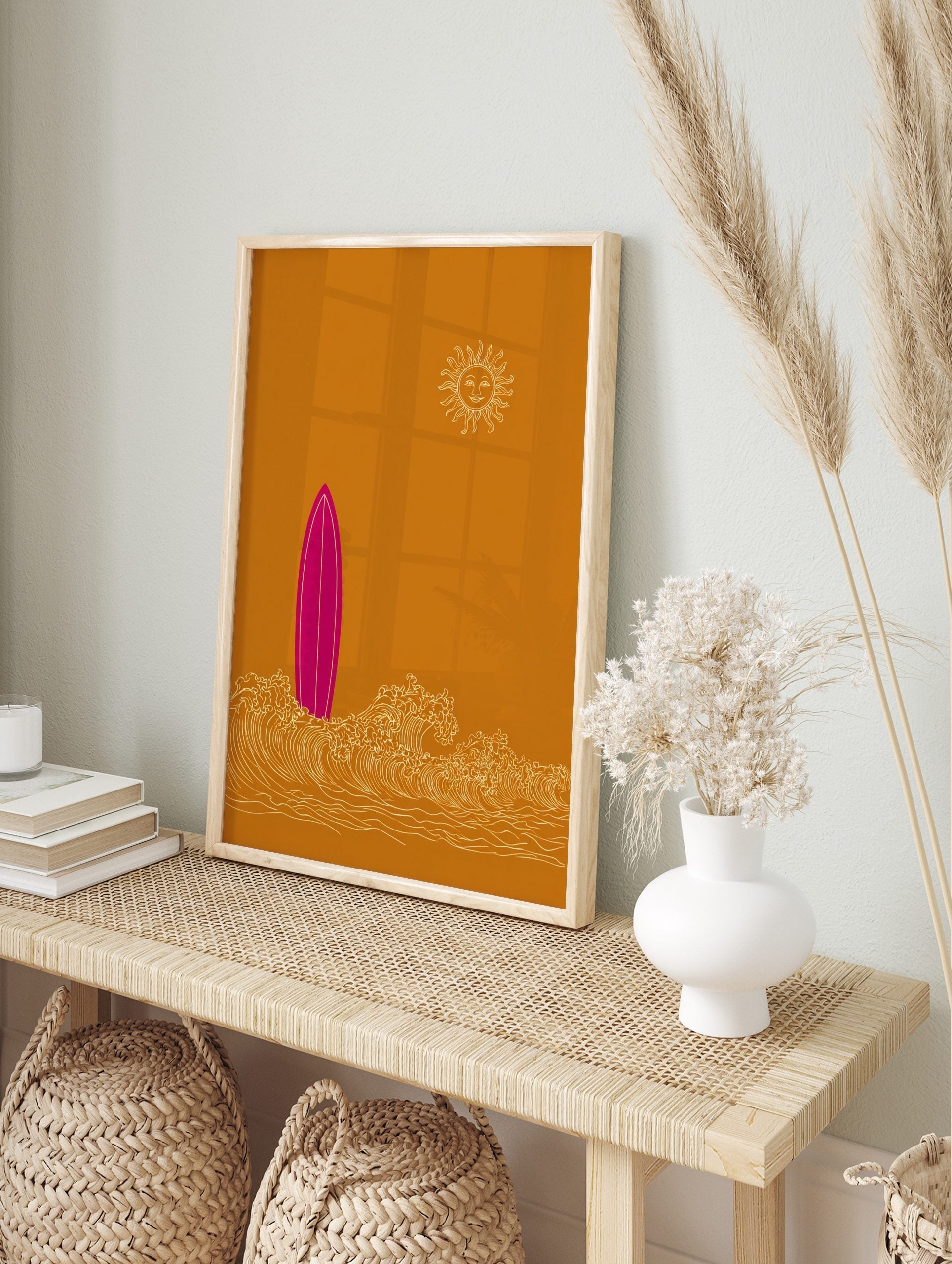 Pink surfboard standing in white ocean waves with a smiling sun on an ochre background in an, in an alternate framed mockup