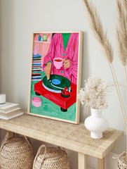 Illustration of a person in a pink coat with tea and a red record player on a green surface, in an alternate framed mockup