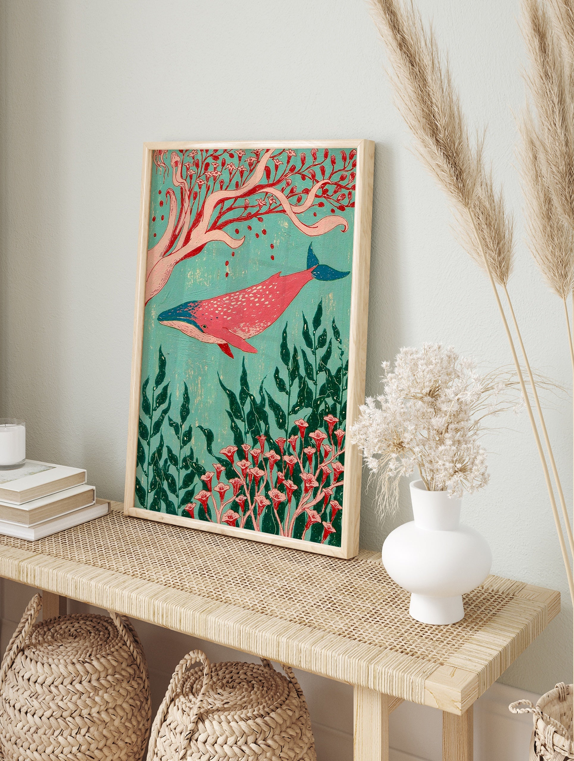 Pink whale swimming among red botanical flowers and green seaweed on a turquoise background, in an alternate framed mockup