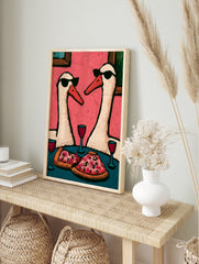 Two swans wearing sunglasses eating pizza and drinking red wine on a pink background, in an alternate framed mockup