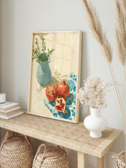 Pomegranate wall art with two red pomegranates, one cut, on a blue patterned cloth next to a blue vase with green leaves. - Image 3