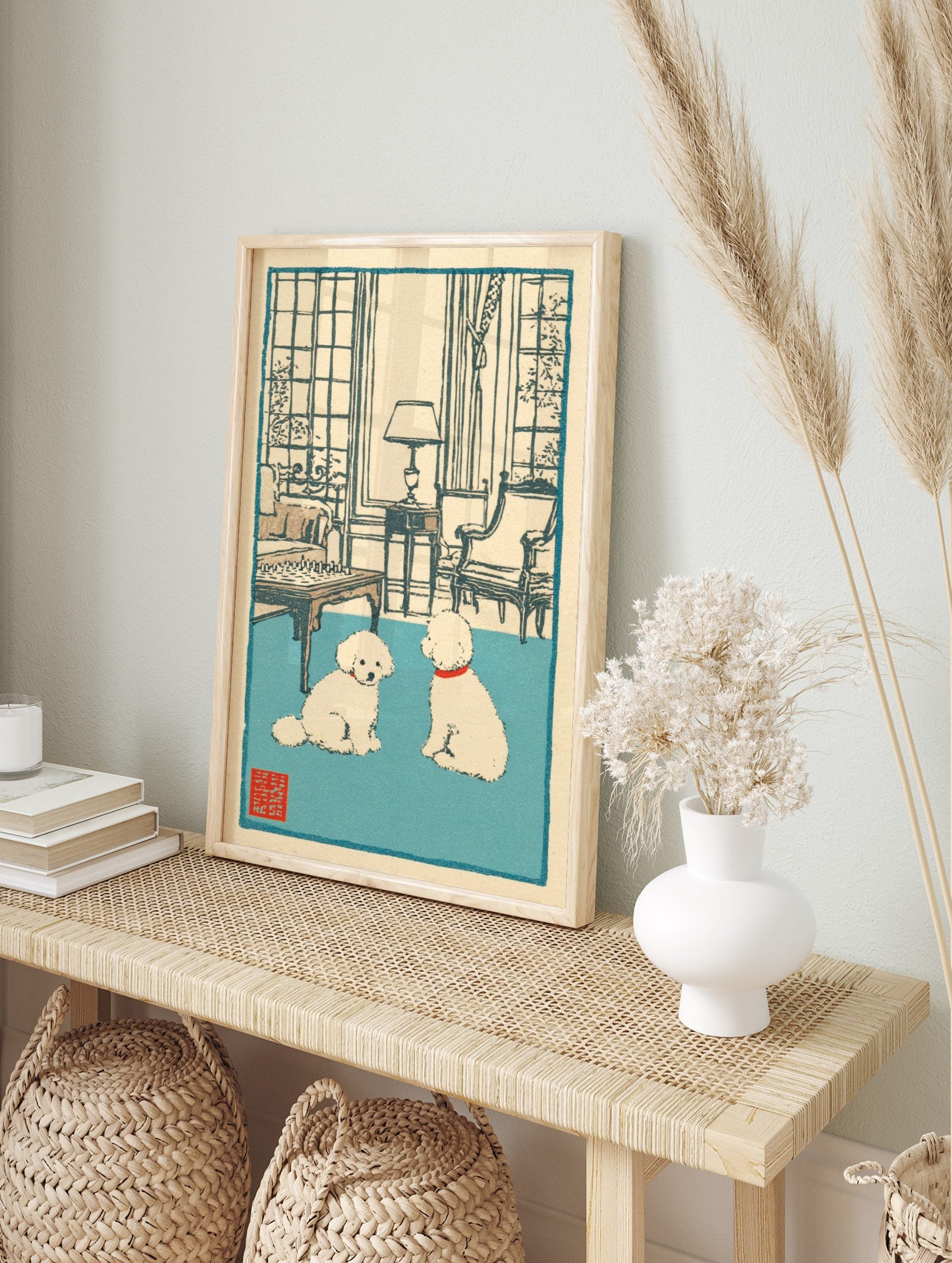 Illustrative print of two white poodles with red collars on a blue rug in a room with a, in an alternate framed mockup