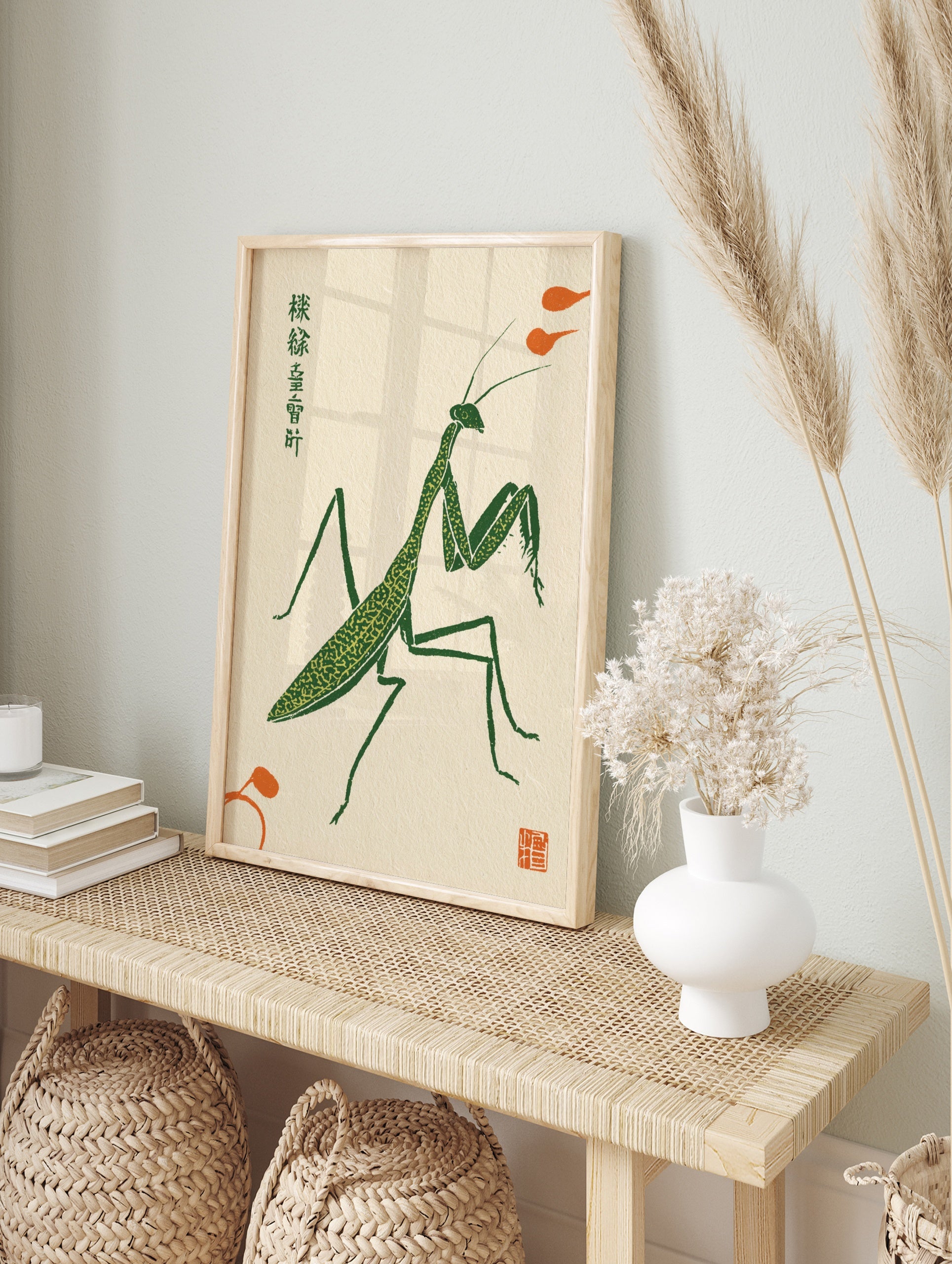 Stylised green praying mantis illustration in a woodblock print style with orange accents on, in an alternate framed mockup