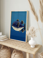 Illustrative puffer fish with blue, white spots, red eye, yellow fins against blue striped, in an alternate framed mockup