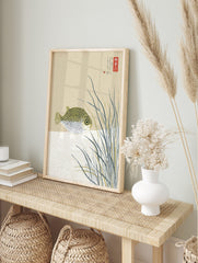 Illustrative pufferfish with black spots among tall grasses and Japanese text on a beige, in an alternate framed mockup
