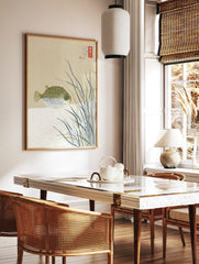 Illustrative pufferfish with black spots among tall grasses and Japanese text on a beige background, in a styled room mockup