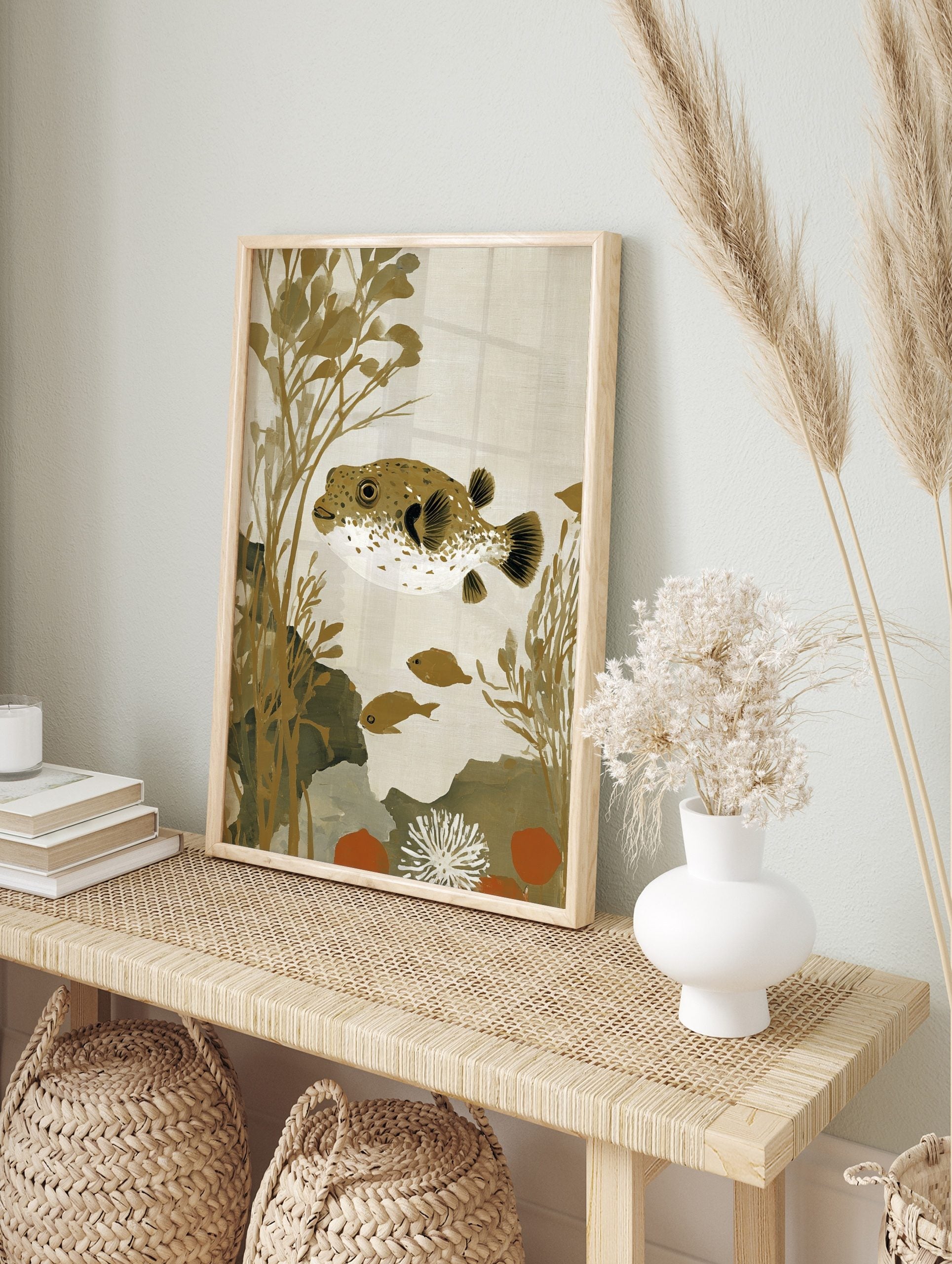Illustrative pufferfish with brown spots and white underside, swimming amongst golden seaweed, in an alternate framed mockup