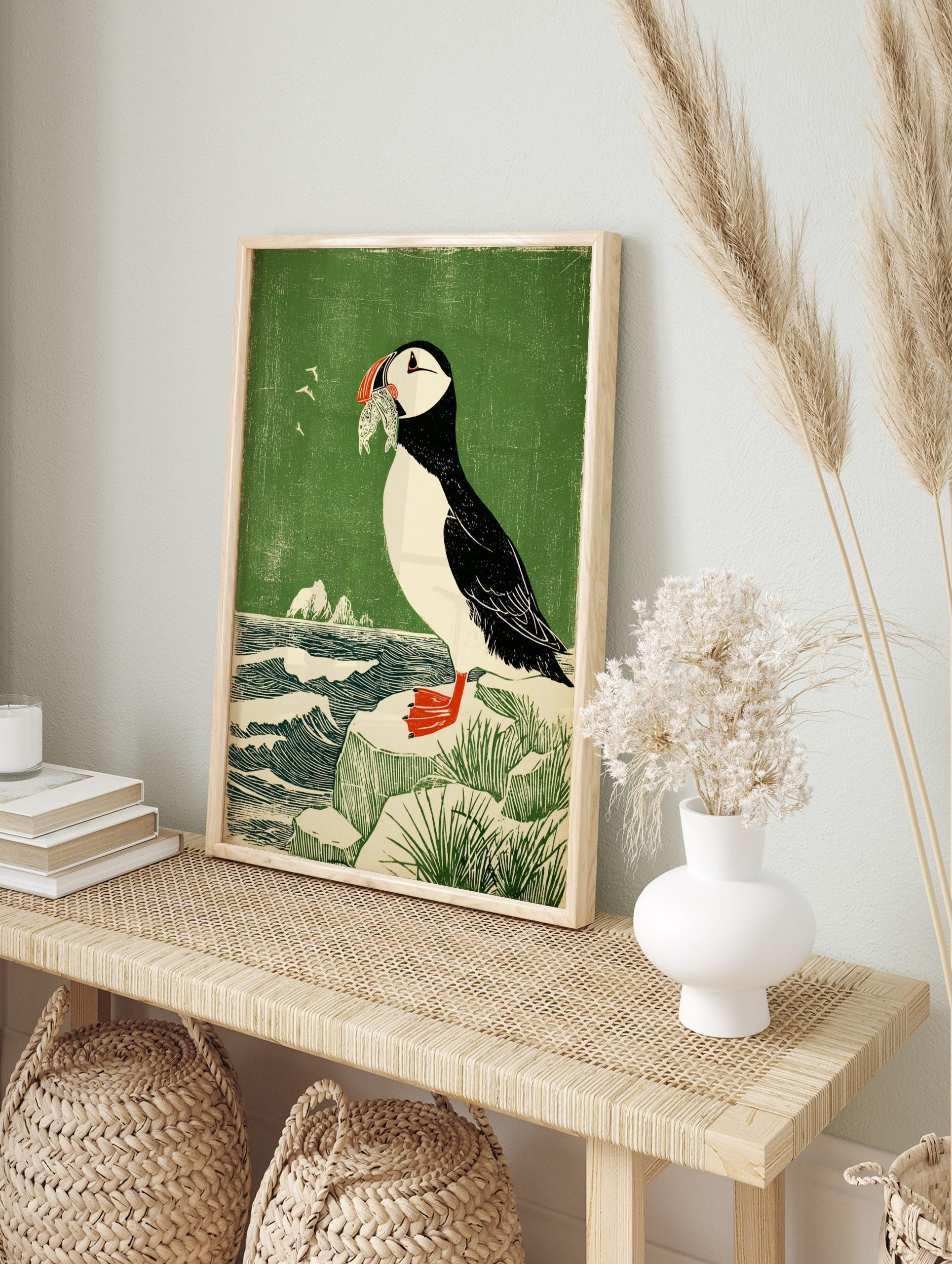 Illustrative woodcut style print of a puffin holding fish in its beak, standing on a rock by, in an alternate framed mockup