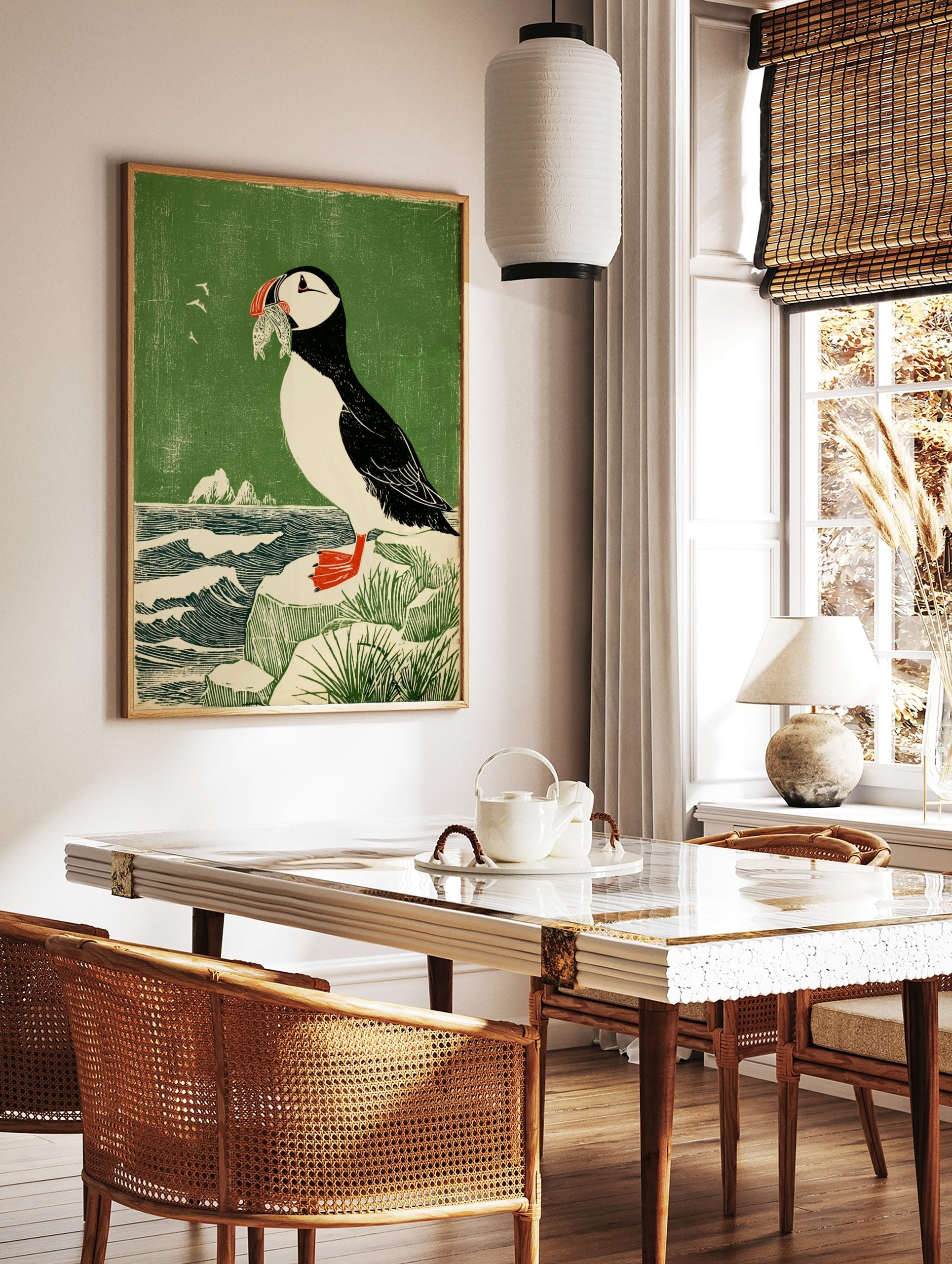 Illustrative woodcut style print of a puffin holding fish in its beak, standing on a rock by a, in a styled room mockup