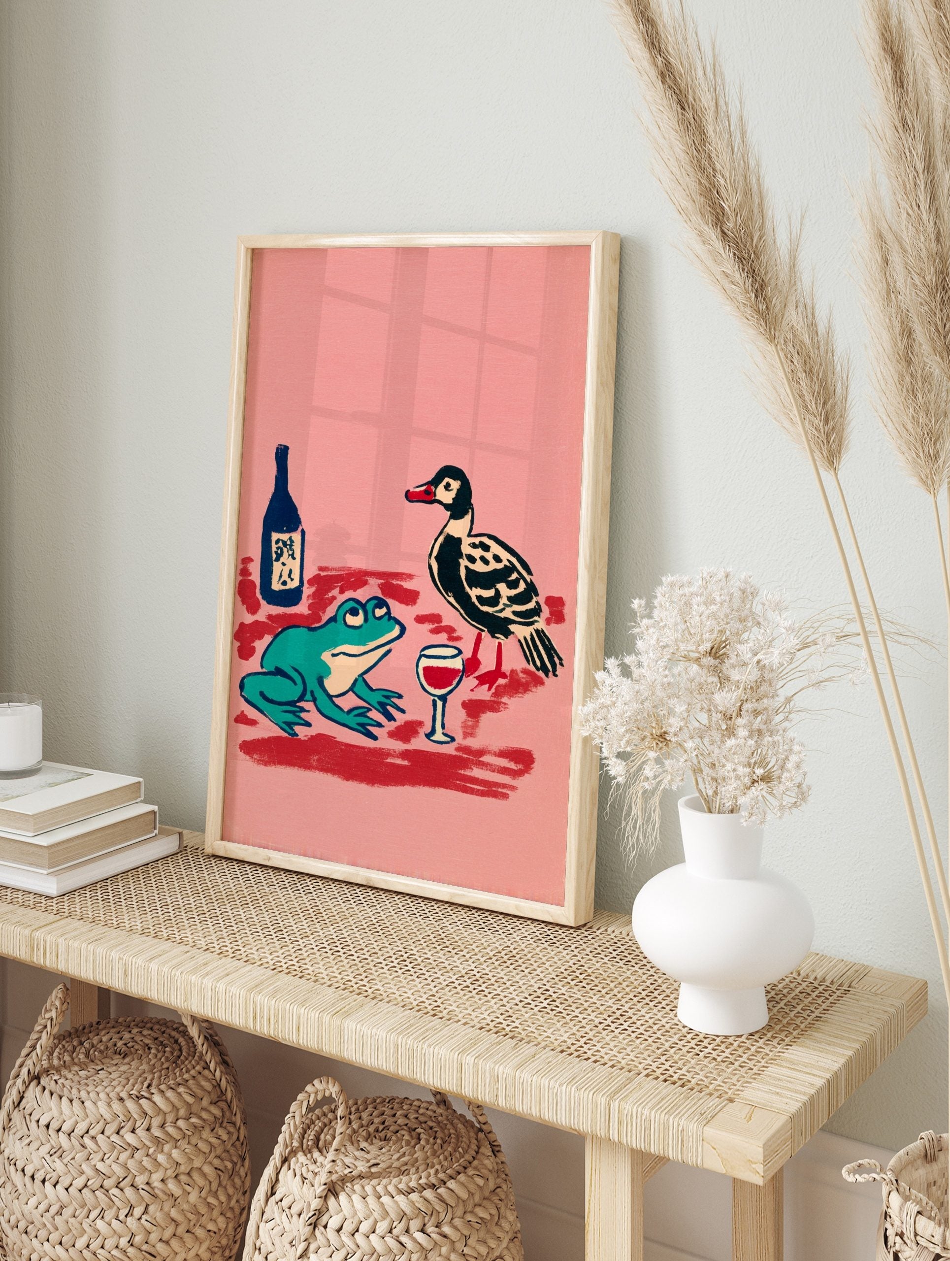 Illustrative print of a teal frog and black duck with a wine glass and bottle on a pink, in an alternate framed mockup