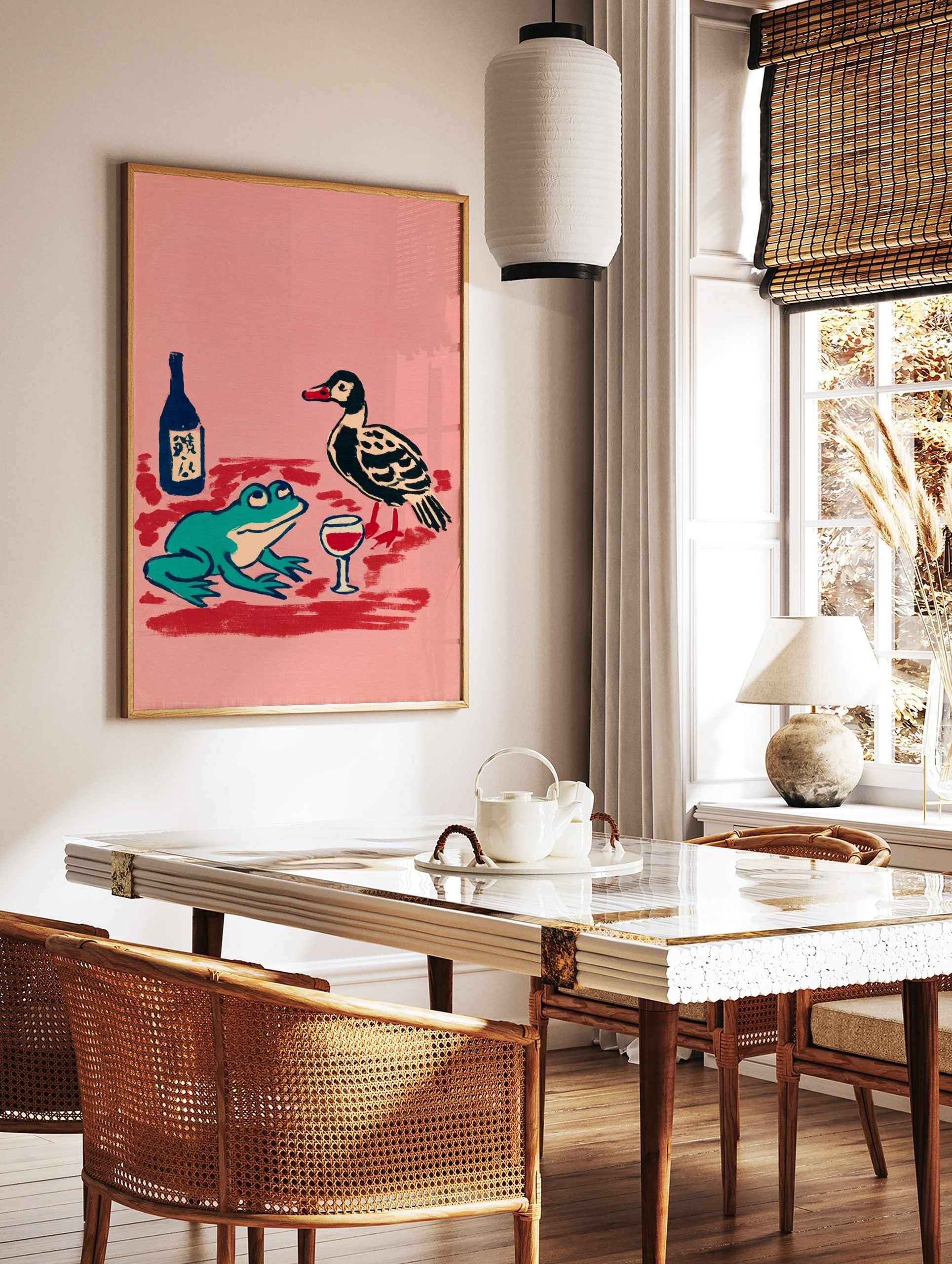Illustrative print of a teal frog and black duck with a wine glass and bottle on a pink background, in a styled room mockup