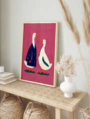Illustrative art print of two white geese, one in a blue coat, against a textured pink, in an alternate framed mockup