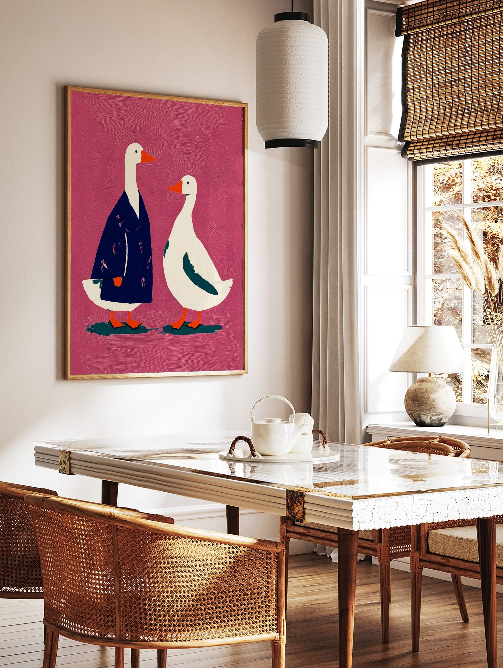 Illustrative art print of two white geese, one in a blue coat, against a textured pink background, in a styled room mockup