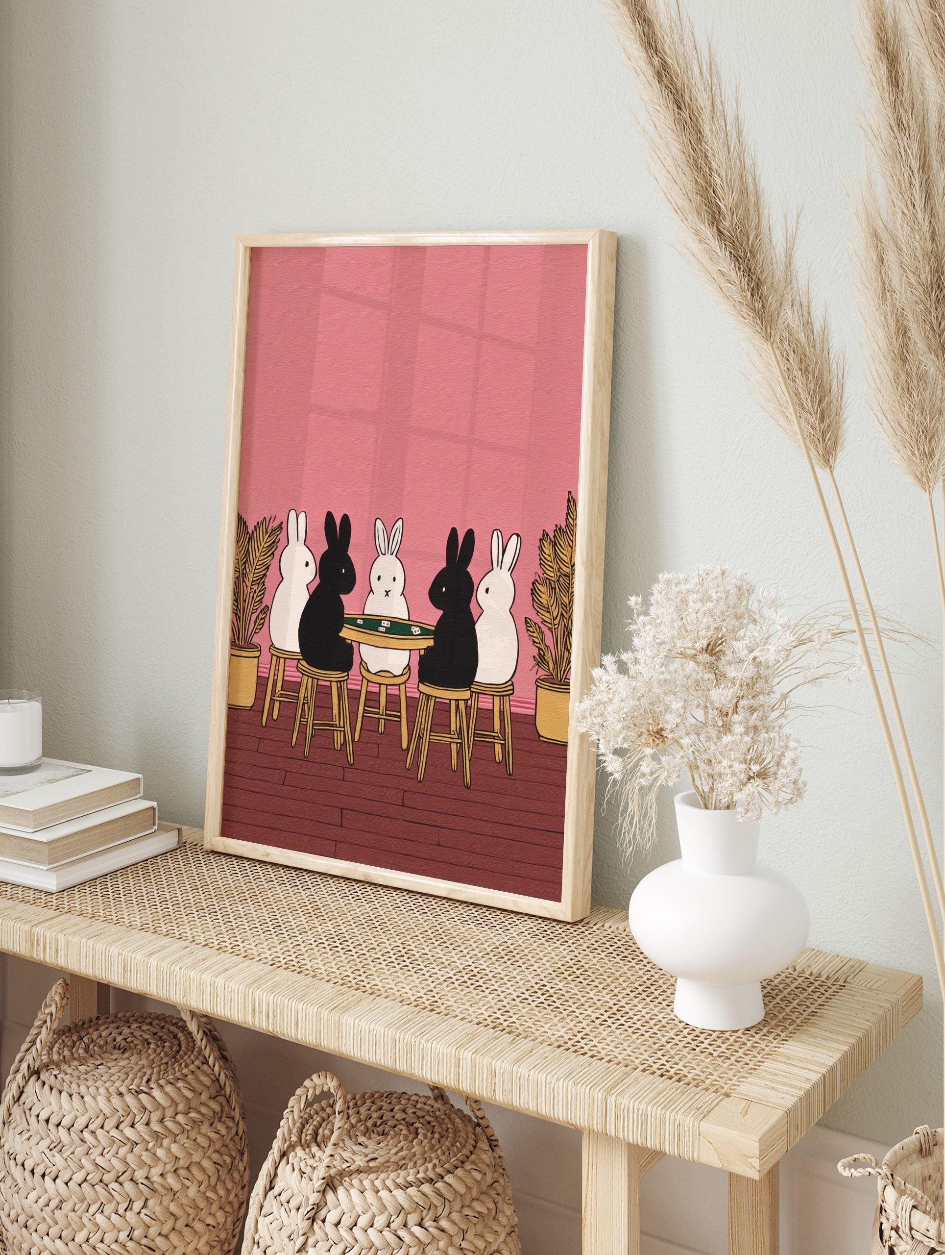 Illustrative print of five black and white rabbits playing cards at a green table on a pink, in an alternate framed mockup