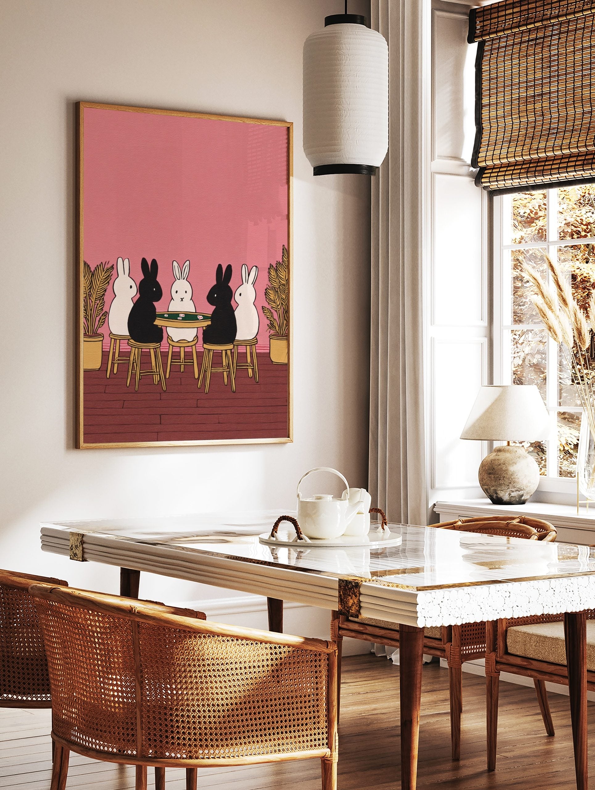 Illustrative print of five black and white rabbits playing cards at a green table on a pink, in a styled room mockup