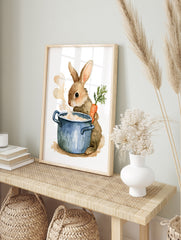 Watercolor illustration of a fluffy brown rabbit holding a carrot next to a steaming blue, in an alternate framed mockup