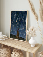 Illustrative rabbit silhouette gazing up at falling golden stars against a textured deep blue, in an alternate framed mockup