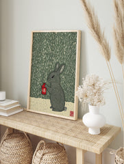 Illustrative woodcut style print of a grey rabbit holding a red lantern in the rain, dark, in an alternate framed mockup