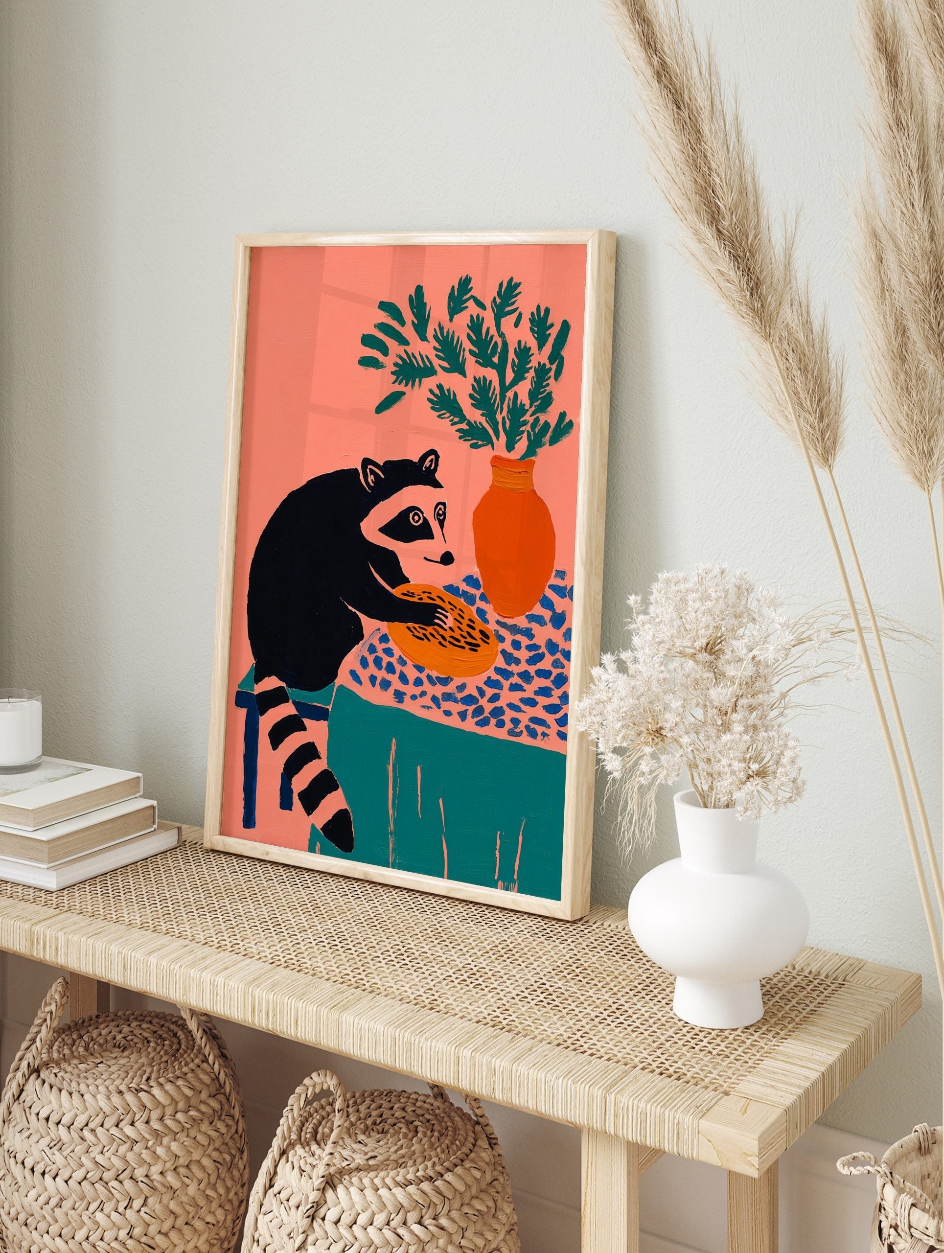 Illustrative raccoon holding a pie on a patterned tablecloth with a vase of green foliage, in an alternate framed mockup