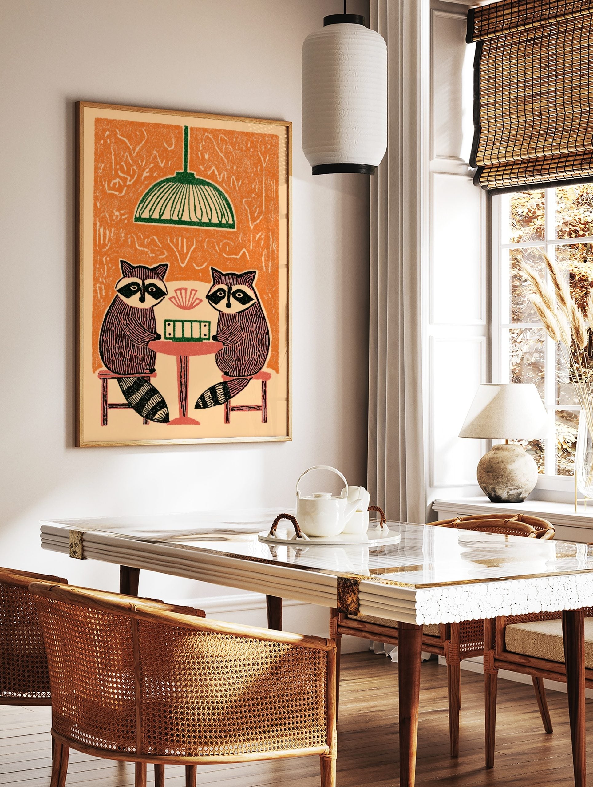 Illustrative print of two raccoons playing cards at a table under a green lamp, with an orange, in a styled room mockup