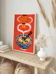 Ramen bowl illustration with a hanging lantern and chopsticks on a vibrant red background, in an alternate framed mockup