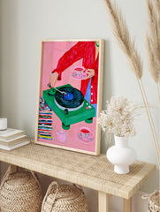 Vivid illustration of a person with a green record player, floral teacup, and vinyl stack, in an alternate framed mockup