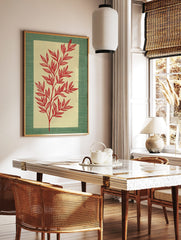 Red botanical illustration of a leafy stem on a pale beige panel, framed by a textured green border, in a styled room mockup