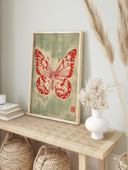 Red butterfly illustration with detailed wings and antennae on a textured greenish-blue, in an alternate framed mockup
