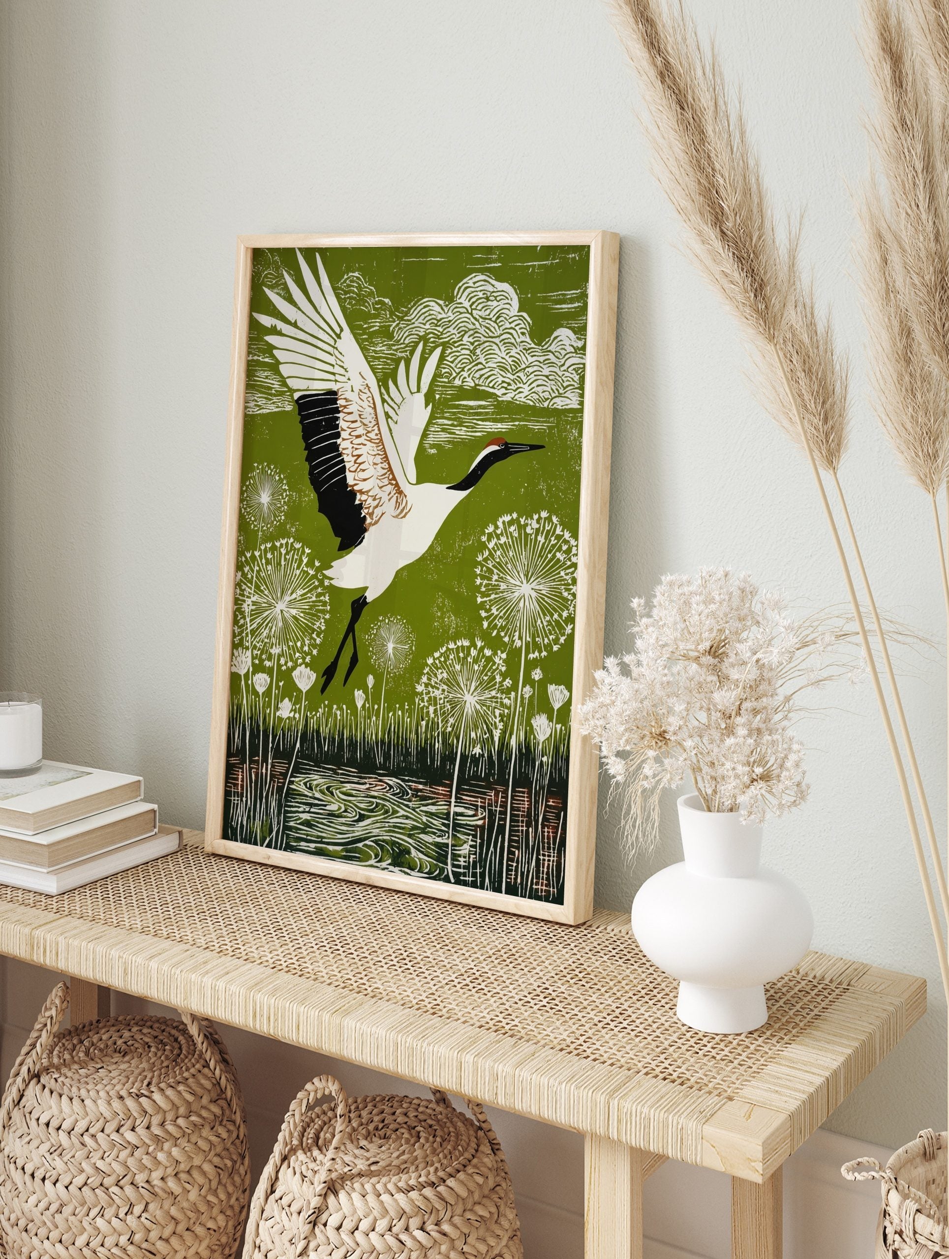 Red-crowned crane in flight over green landscape with white dandelion seed heads and water, in an alternate framed mockup