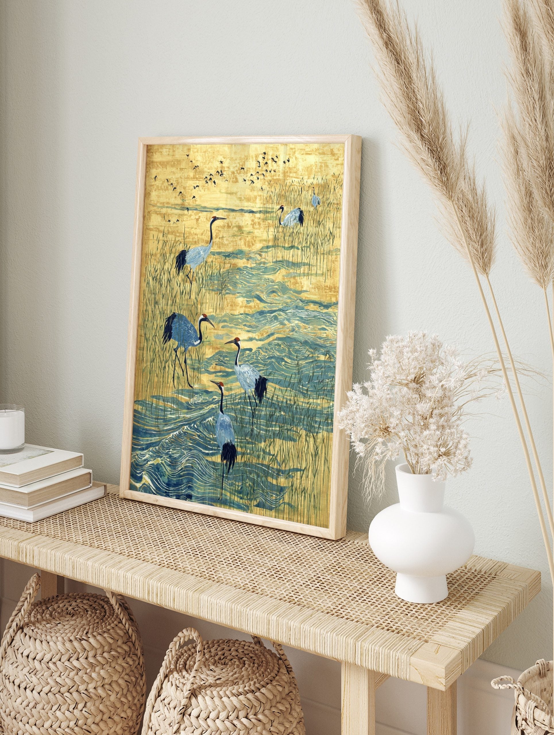 Illustrative print of red-crowned cranes wading in blue water amongst golden reeds with, in an alternate framed mockup