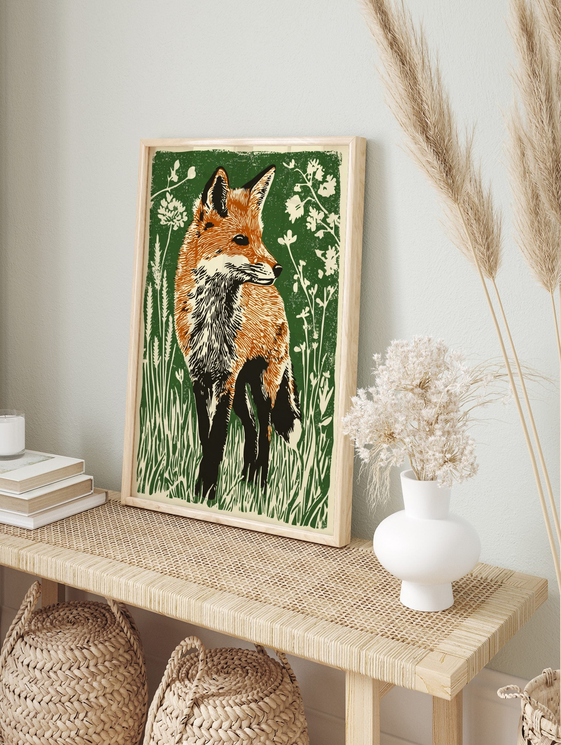 Illustrative linocut style print of a red fox with orange fur in green grass and white flowers, in an alternate framed mockup