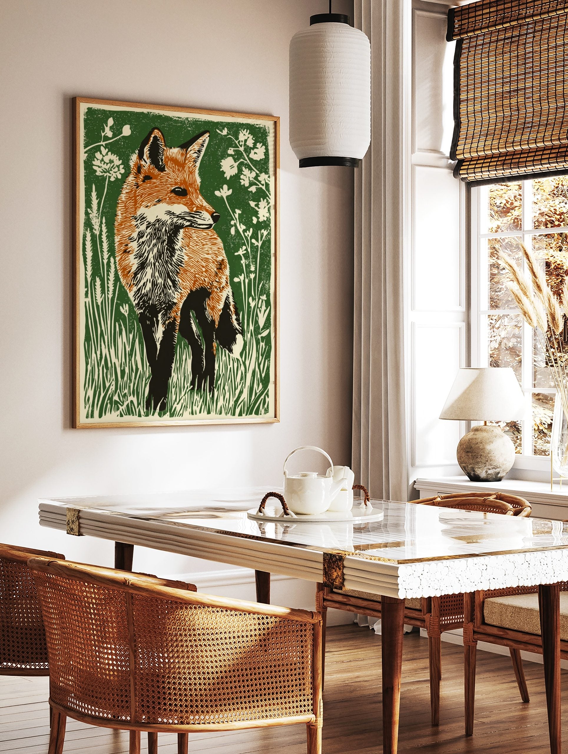 Illustrative linocut style print of a red fox with orange fur in green grass and white flowers, in a styled room mockup