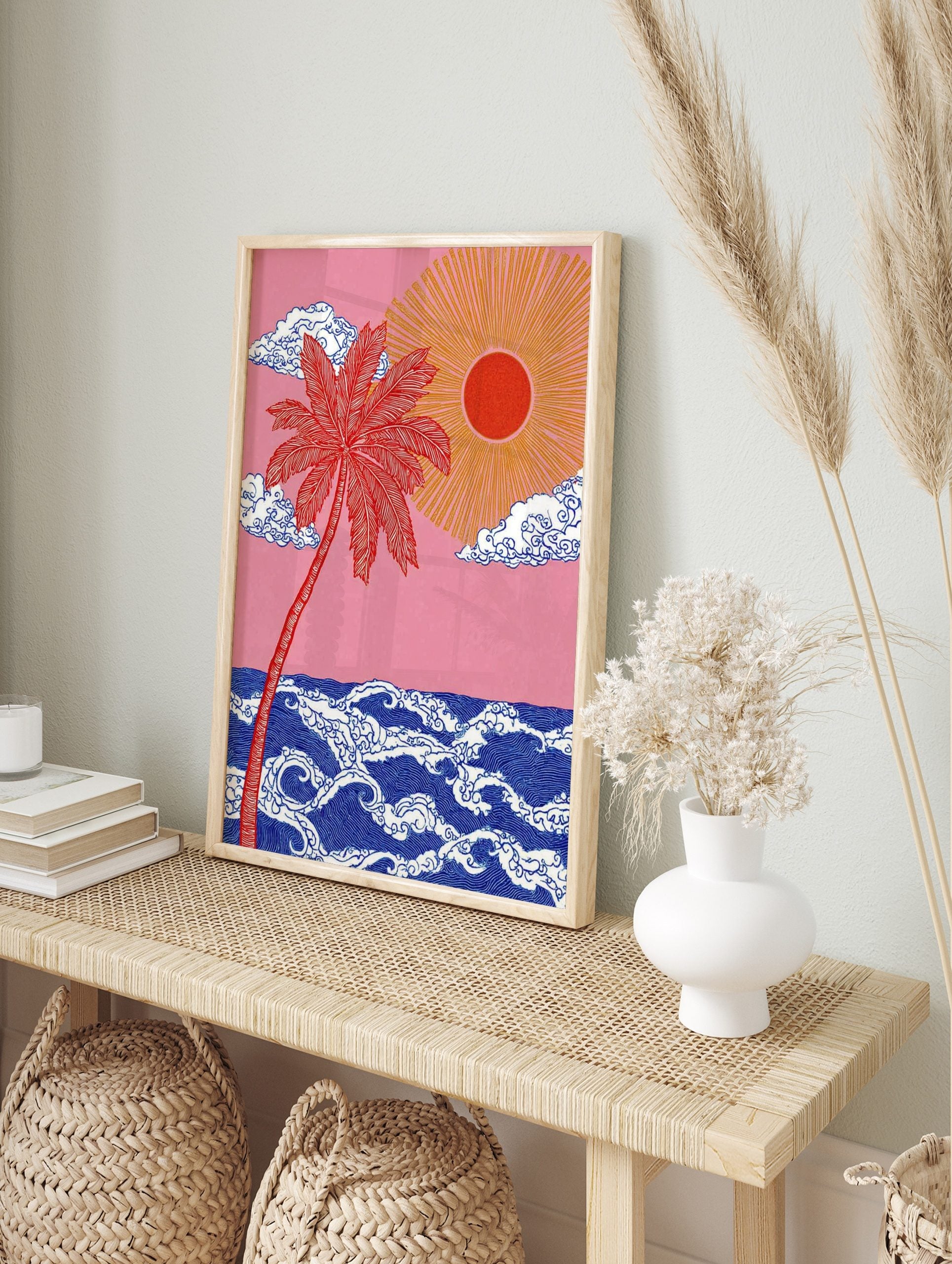 Red palm tree and golden sun over stylised blue ocean waves against a pink sky, illustrative, in an alternate framed mockup