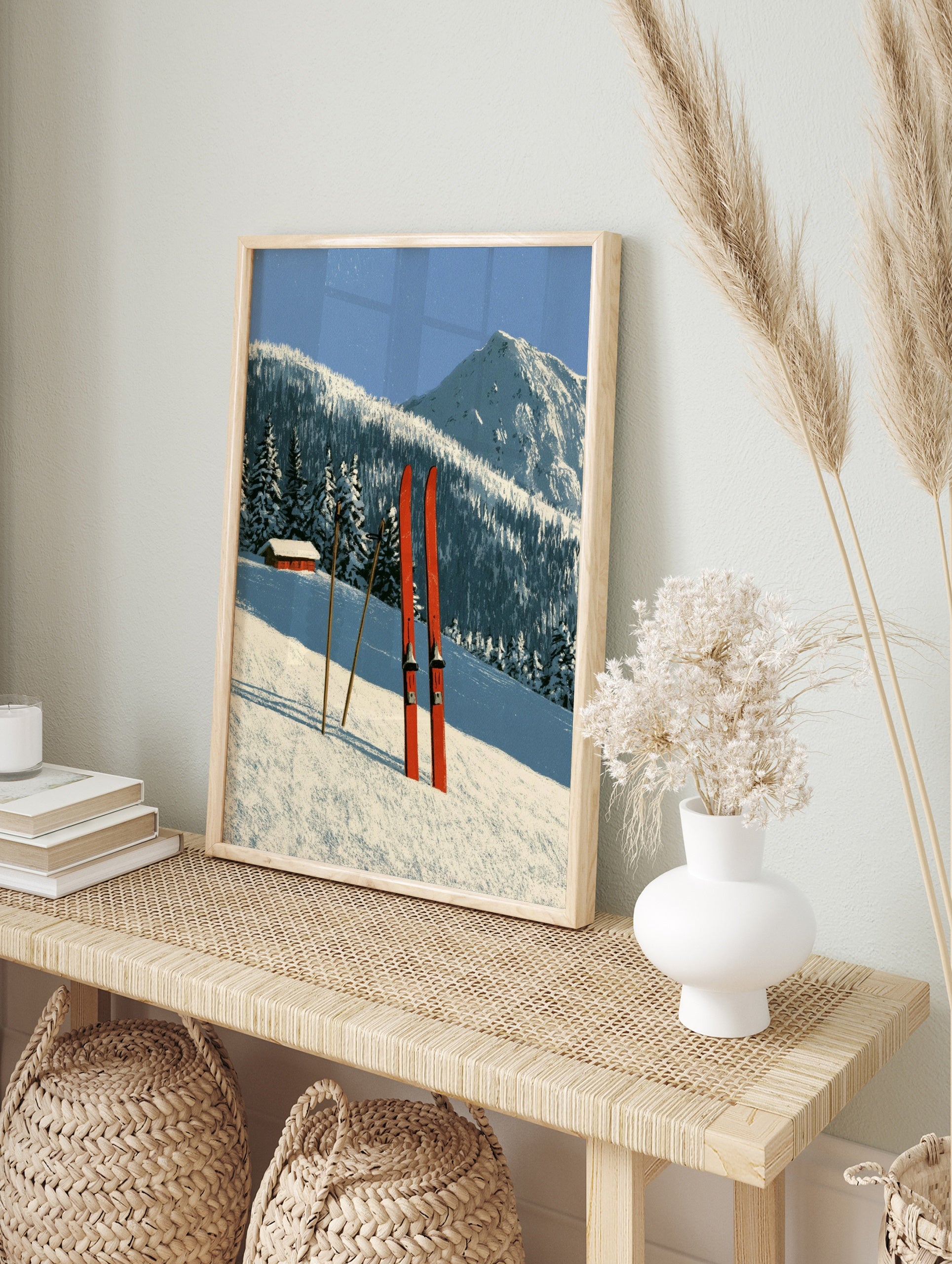 Red skis and poles in deep snow with a mountain cabin and forest background illustration, in an alternate framed mockup