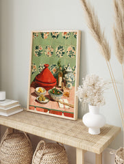 Red tagine pot, lemons, olives, salad, oil bottles, and patterned jar on pink table with, in an alternate framed mockup