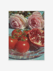 Poster of glistening red tomatoes, pink roses, and a sliced pomegranate on a clear glass plate with a blue background and glitter.