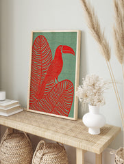 Red toucan with large bill perched on a striped tropical leaf against a textured teal, in an alternate framed mockup