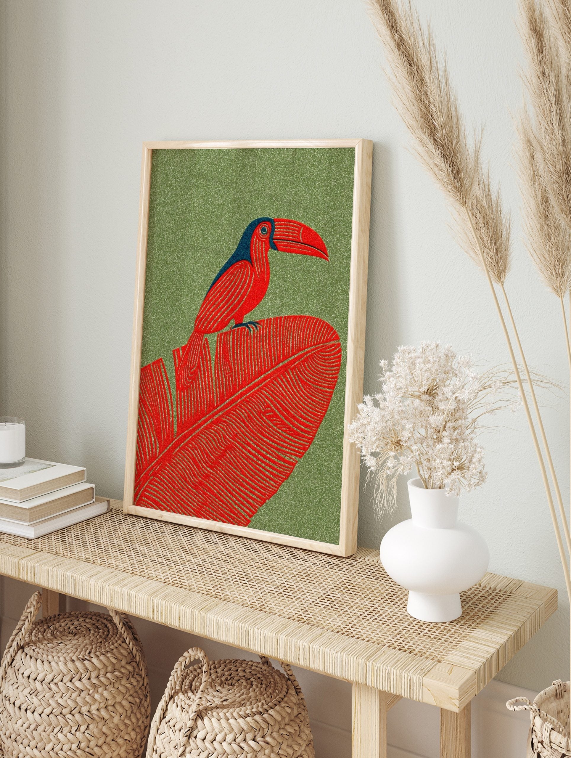 Red toucan with blue head perched on a large red tropical leaf against a green textured, in an alternate framed mockup