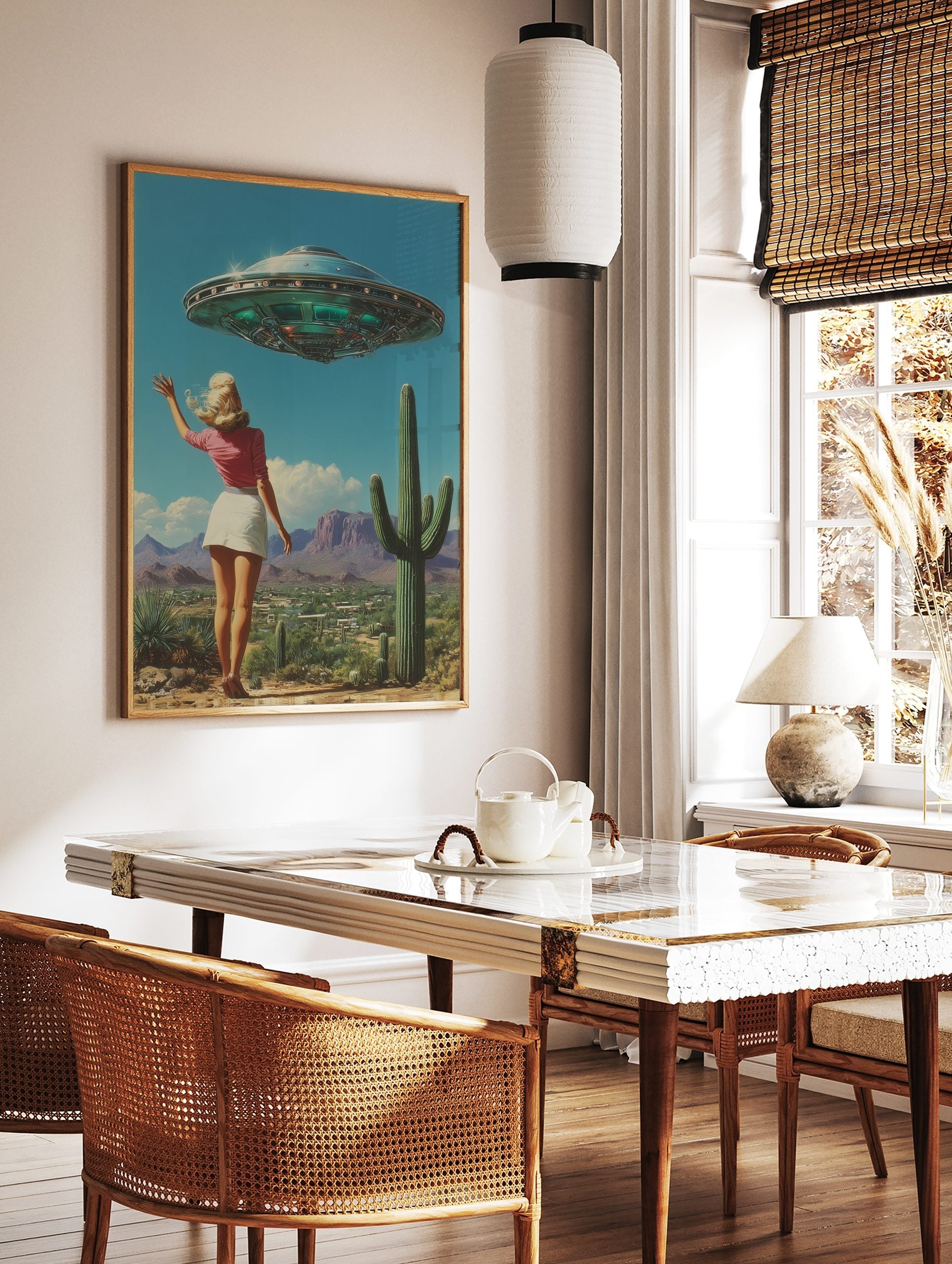 Retro UFO desert wall art featuring a woman waving at a flying saucer above a landscape with cacti and mountains, displayed as the same artwork in a styled poster mockup for home decor
