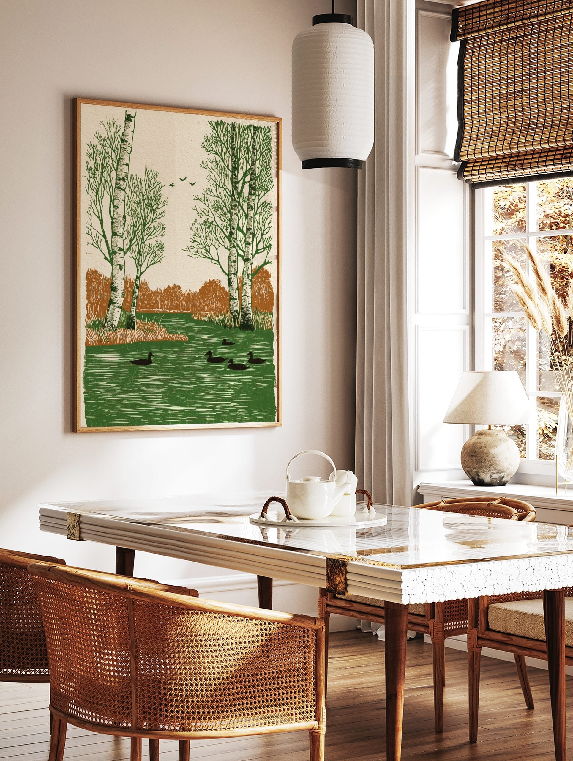 Woodcut style art print of birch trees and ducks swimming in a green river with brown foliage, in a styled room mockup