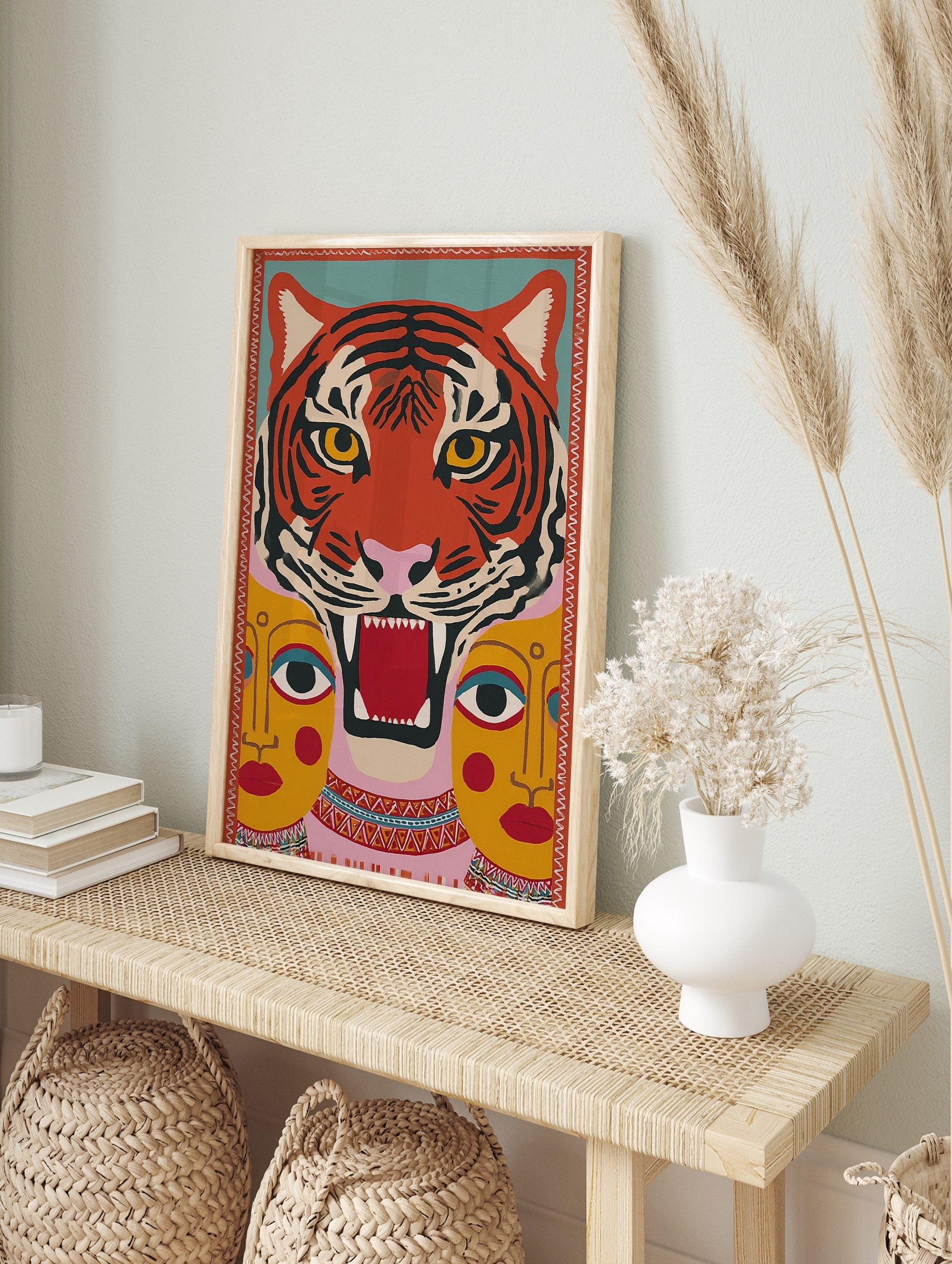 Stylised roaring tiger face with two yellow human faces below, in a vibrant folk art inspired, in an alternate framed mockup
