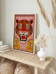 Stylised roaring tiger face with yellow eyes and two abstract human faces on a pink, in an alternate framed mockup