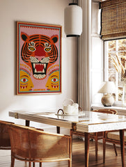Roaring tiger head folk art print with black stripes, yellow eyes, red mouth, pink background, and, in a styled room mockup