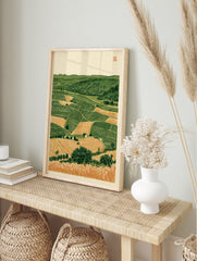 Rolling countryside landscape with patchwork fields, green hills, and foreground wheat, in an alternate framed mockup