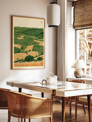 Rolling countryside landscape with patchwork fields, green hills, and foreground wheat stalks, in a styled room mockup